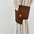 Close-up view of a Nordic style brown PU leather curtain tieback with a metal snap button detail. - Dark Brown
