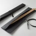 Black leather drumstick roll bag detail showing texture, strap and wooden drumsticks inside. - Black