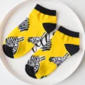 Close-up detail of yellow and black ankle socks featuring playful zebra head patterns. - Zebra / Yellow Zebra