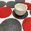 Detailansicht der roten und grauen runden Filzuntersetzer mit weisser Tasse auf Tisch. - Rund / Rot