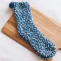 Close-up detail of cozy blue fleece floor socks with cute pom-pom, soft winter sleep sock texture. - Blue White Granule