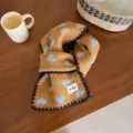 Vue détaillée de l'écharpe en tricot confortable avec des cœurs bleus et une bordure marron. - Cœur Surjeté / Chameau Foncé