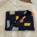 Vue détaillée d'une écharpe en tricot douillette avec des blocs géométriques colorés foncés. - Bleu marine