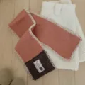 Gros plan détail de l'écharpe en tricot color-block avec étiquette et bord blanc. - Café Pamplemousse