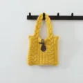 Gros plan détaillé sur la texture en tricot torsadé du sac à main jaune et son attache. - Style Torsades Bouton / Jaune