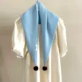 Vue détaillée d'une écharpe triangulaire en tricot bleu clair avec des pompons. - Bleu clair