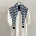 Vue détaillée d'une écharpe triangulaire en tricot rayé gris avec des pompons. - Gris Rayé