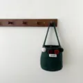 Vue détaillée d'un élégant sac seau en feutre vert foncé avec des pompons colorés. - Vert Fruit
