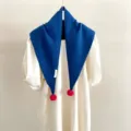 Vue détaillée d'une écharpe triangulaire en tricot 100% laine avec de beaux pompons roses. - Bleu