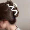 Vista detallada de la gran pinza de pelo mate y ondulada usada, elegante accesorio de moda. - Blanco Roto Esmerilado