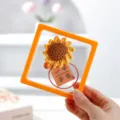 Primo piano di un portachiavi girasole all'uncinetto fatto a mano con biglietto d'auguri in cornice. - Ciondolo Finito (Punteggio Massimo + Scatola Sospesa)
