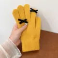 Close-up detail of warm yellow knit gloves with cute black velvet bows and pearl decoration. - One Size / Yellow
