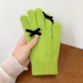Close-up detail of green knit five-finger gloves with black velvet bows, winter warm accessory. - One Size / Green