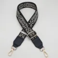 Detailed view of the wide black embroidered bag strap with golden metal hardware and hooks. - Black Beige + Black Leather