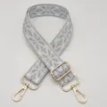 Primo piano della tracolla ricamata geometrica grigia con accessori in metallo dorato. - Bianco e Grigio Chiaro