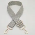 Primo piano della tracolla per borsa in tessuto jacquard con motivo geometrico e parti dorate. - Grigio medio su fondo beige
