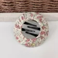 Dettaglio della molletta per capelli rotonda in tessuto floreale, elegante accessorio quotidiano. - fiori rosa