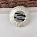 Beige pleated fabric round hair clip detail, featuring black inner combs for secure bun styling. - Off White