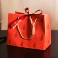 Rote Papiertüte mit Tannenbaum-Muster, goldenen Kordeln und edler roter Schleife als Geschenk. - S / Roter Glücksbaum