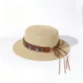 Flat top straw sun hat detail showing ethnic woven band with metal coin pendants and leather bow. - One Size (Circumference 57cm) / Metal Coin Wreath - Beige