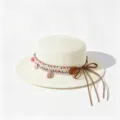 Closeup view of a flat top straw hat featuring boho woven band and elegant brown ribbon detail. - One Size (Circumference 57cm) / Pink Tassel Wreath - Creamy White