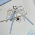 Close-up detail of a charming pearl bow keychain with a cute blue ribbon and silver heart charm. - Blue Bow - Heart Clasp