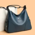Nahaufnahme der blauen Leder Schultertasche mit Metall-Logo und Reißverschlusstasche. - Blau