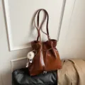 Glänzende braune Schulter-Tragetasche mit Kordelzug und süßem flauschigen Anhänger für den Damenalltag - Mit Anhänger / Braun
