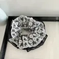 Vue détaillée d'un chouchou en dentelle blanche et tulle noir avec une broderie raffinée. - Noir