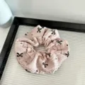 Close-up of the pink lace scrunchie with black bows, showcasing the delicate fabric details. - Pink