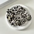 Close-up view of stylish leopard print satin hair scrunchie on decorative white tray. - Leopard Style 5