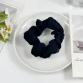 Close up photo of a black silk hair scrunchie placed on a white plate with floral decor. - Elegant Black