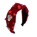 Close-up of red velvet headband featuring sparkling rhinestones, floral details, and skull charms. - Red
