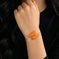 Close-up detail shot of the stylish open gold metal bracelet with vibrant orange enamel drops. - Orange