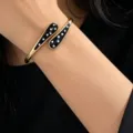 Close-up of gold-tone open bangle with black enamel white polka dot details on wrist. - Black and White