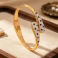 Detail view of gold-tone open cuff bracelet with white enamel and black dot oil-drop design. - White Black