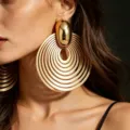 Close-up detail shot of statement gold metal concentric circle earrings worn by a model. - Earrings / Gold