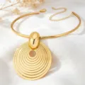 Close-up detail of a bold gold metal choker necklace featuring a large concentric ring pendant. - Choker Necklace / Gold