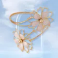 Close up view of the golden arm cuff featuring hollow floral design with pink petals. - Off White
