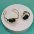 Elegant gold-tone cuff bracelet and adjustable ring set featuring bold black oval stones. - Ring Bracelet Set / Black