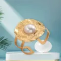 Gold-plated hammered texture bangle bracelet featuring a large central pearl, elegant design. - White