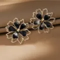 Detailed close-up shot of double-layered hollow flower earrings with black enamel and gold outline. - Black
