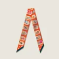 Gedetailleerd opname van een stijlvolle oranje smalle twilly sjaal met artistieke illustraties. - Oranje