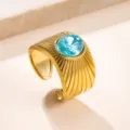 Primer plano de anillo ancho de acero inoxidable dorado con líneas talladas y una piedra de circonio. - Talla única / Azul