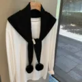 Detail shot of black knit triangular scarf with pom poms layered on white long sleeve tee. - Black