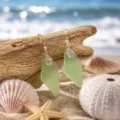 Handcrafted sea glass earrings with silver hooks and wire wrap on driftwood beach background. - Green Wire-Wrapped Earrings (24043004)