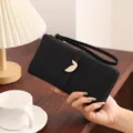 Detail shot of black PU long wallet featuring gold leaf buckle, zipper and convenient wrist strap. - Black