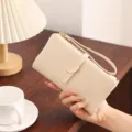 Close-up of beige long wallet featuring elegant leaf metal buckle and convenient wrist strap. - Apricot