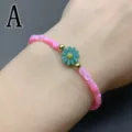 Close-up detail shot of pink beaded bracelet featuring a green flower charm and gold beads. - Letter A