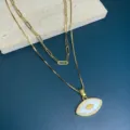 Detail shot of double layer gold necklace featuring mother of pearl evil eye pendant. - White